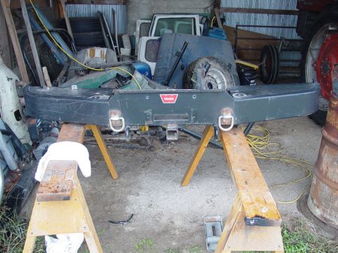 1979 Ford Bronco - This heavy-duty bumper, likely for an off-road vehicle, is supported by sawhorses amidst various automotive parts and equipment.
