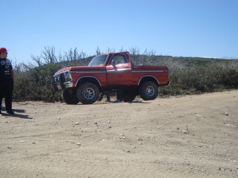 1986 Ford Bronco - Orange 1979 Ford F-150 4x4 pickup truck on a dirt road with scrub brush and clear blue sky.
