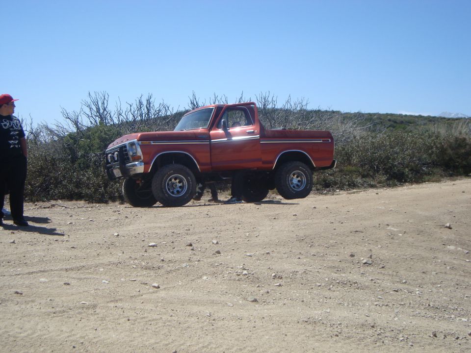Orange 1979 Ford F-150 4x4 pickup truck with lifted suspension on a dirt road