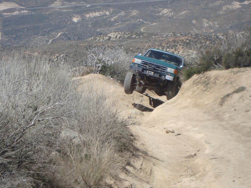 Green SUV going down a steep, rocky trail. Looks like a 1987 Ford Bronco