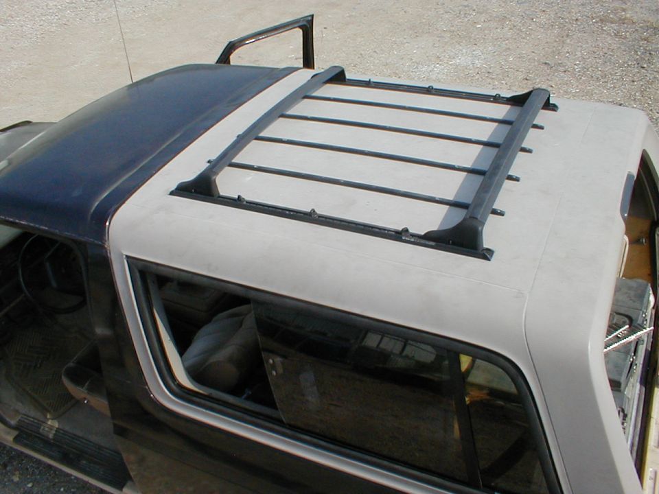 Black-and-gray hardtop with a flat roof rack removed and set on a dirt lot, side window visible