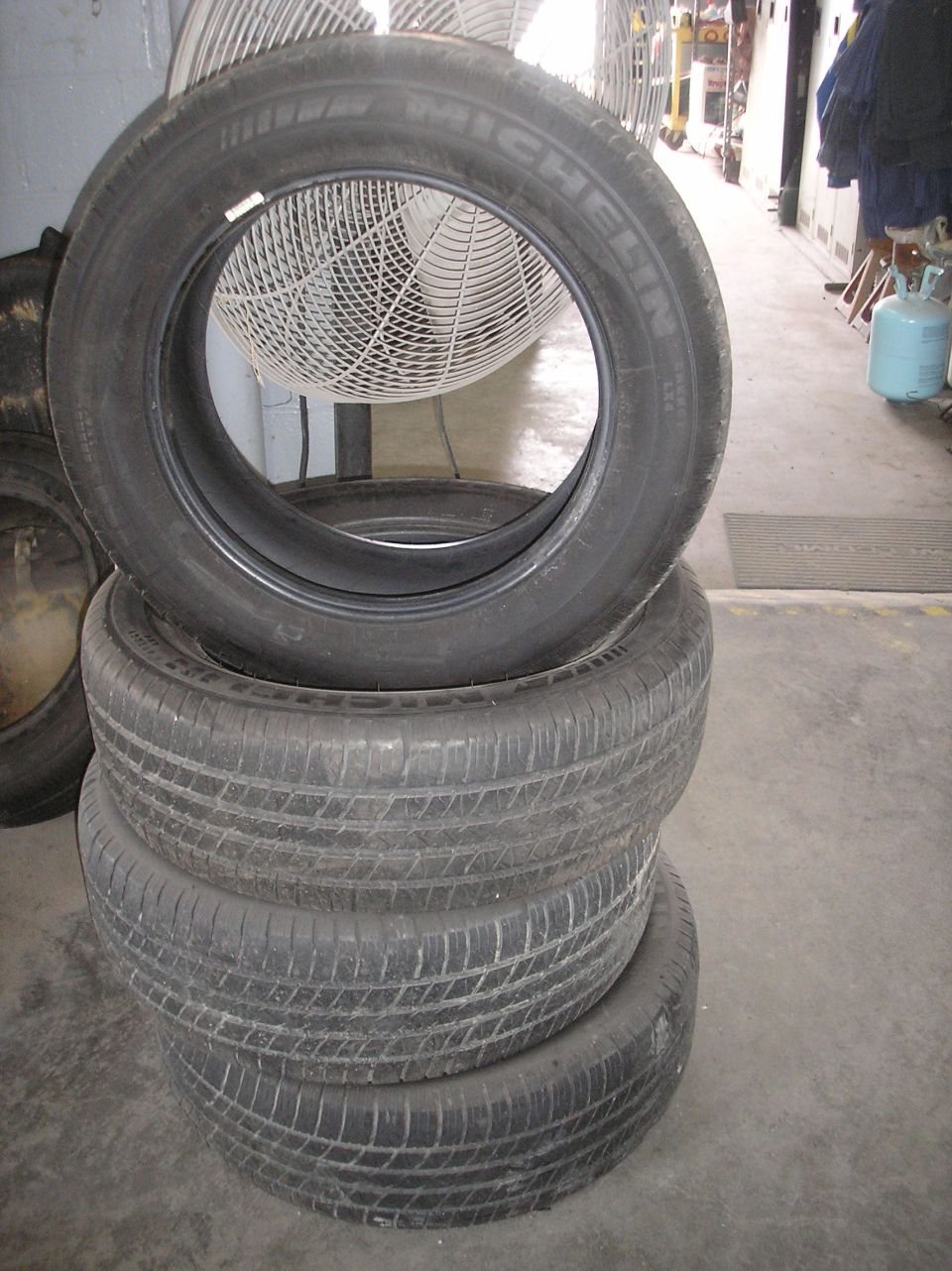 stack of four Michelin tires, one on top of three, in a garage with a fan behind them