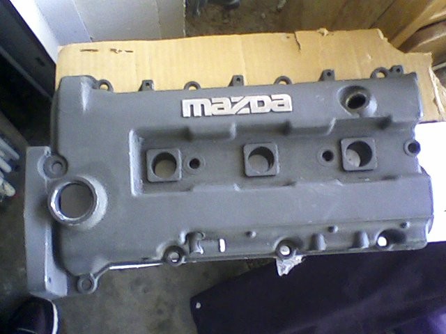 Gray Mazda valve cover with silver lettering, viewed from above
