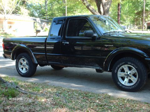 1990 Ford F-150 - A black Ford Ranger pickup truck is parked on a paved surface with grass and trees in the background.