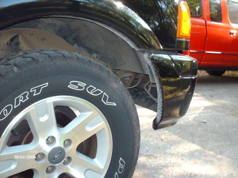 1990 Ford F-150 - Detail shot of a black truck's rear wheel and bumper, with another red truck in the background.
