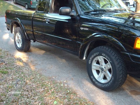 1990 Ford F-150 - Side view of a black Ford Ranger pickup truck, with a green SUV visible in the background.