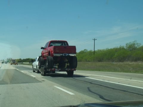 2004 Aston Martin Virage - A red pickup truck is transported on a trailer on a highway.