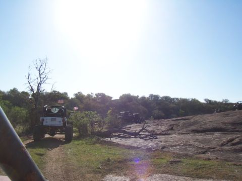 2004 Aston Martin Virage - Off-road vehicles gathered on a rocky hill with trees and a clear blue sky.
