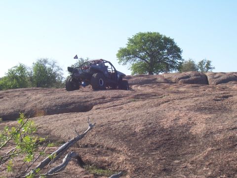 2004 Aston Martin Virage - An off-road buggy navigates a steep, rocky terrain with sparse vegetation and a large tree in the background.