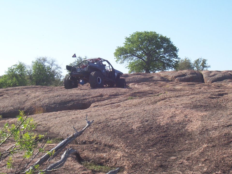 Black off-road buggy with a roll cage and large tires climbing a rocky incline under a clear blue sky