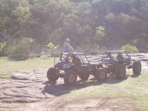 2004 Aston Martin Virage - Two custom-built off-road vehicles are parked in a natural, rocky landscape.