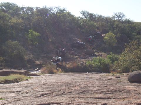 2004 Aston Martin Virage - Several off-road vehicles are seen traversing a challenging rocky terrain on a sunny day.