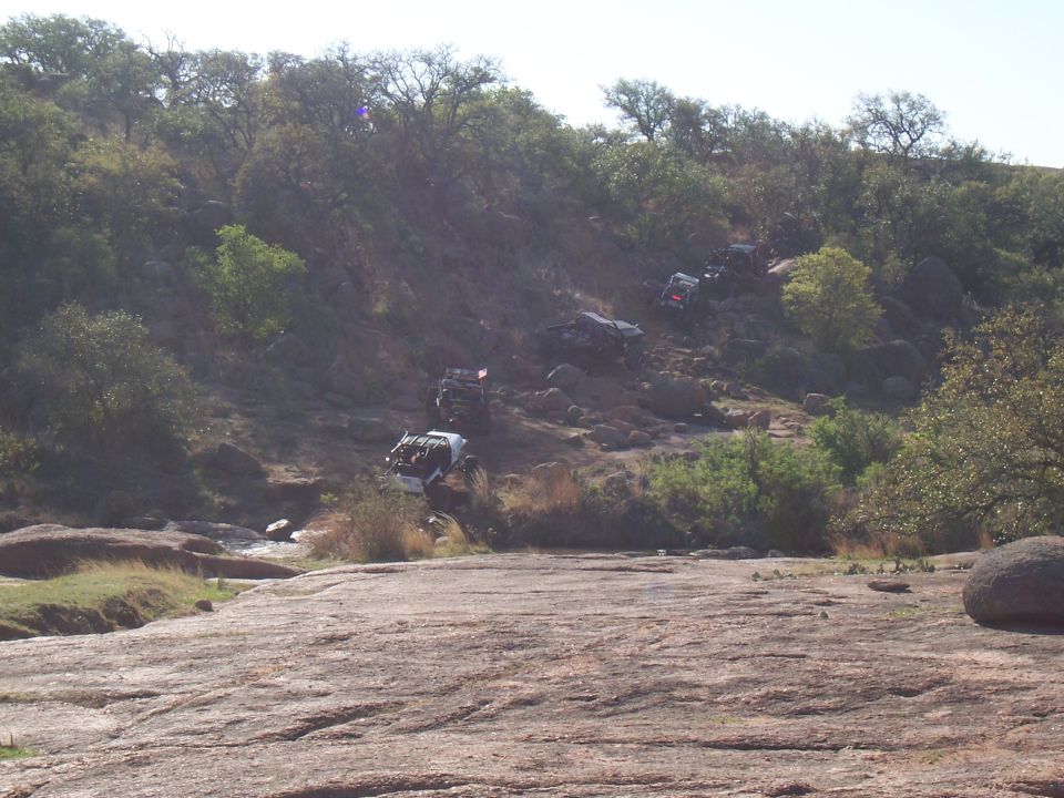 Multiple off-road vehicles navigating a steep, rocky incline with sparse vegetation under a clear sky