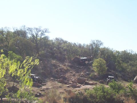 2004 Aston Martin Virage - Multiple off-road vehicles are shown traversing a challenging, rocky incline under a bright sky.