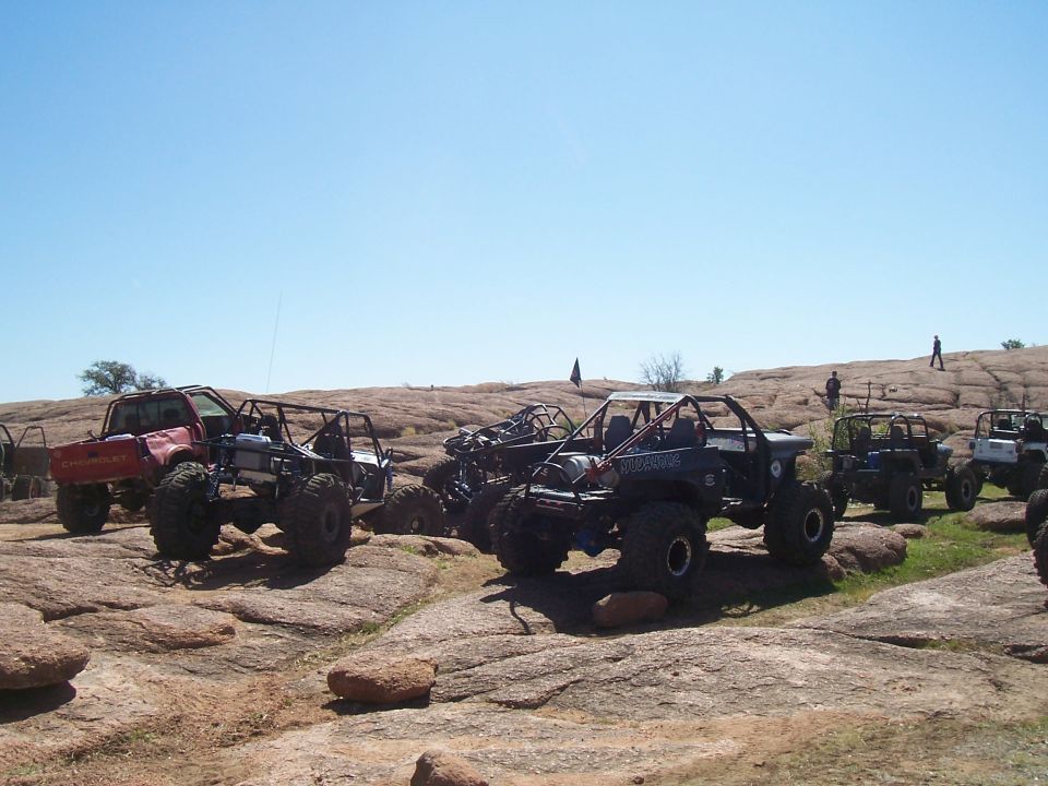 Multiple off-road vehicles parked on a rocky landscape under a clear blue sky