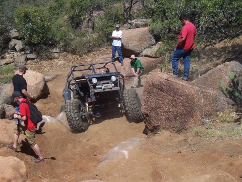 2004 Aston Martin Virage - Off-road buggy navigating a challenging rocky trail with spectators present.