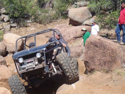 2004 Aston Martin Virage - A custom off-road buggy tackles a challenging rocky terrain with spectators watching.