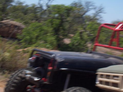 2004 Aston Martin Virage - A black off-road vehicle with a red roll cage is seen next to a tan truck on a dirt path.