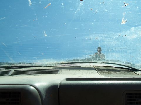 2004 Aston Martin Virage - The dusty dashboard and windshield obscure the view outside, with a person reflected in the glass.