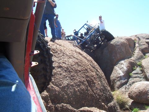 2004 Aston Martin Virage - An off-road buggy is stuck on a steep, rocky terrain, with several onlookers observing the situation.