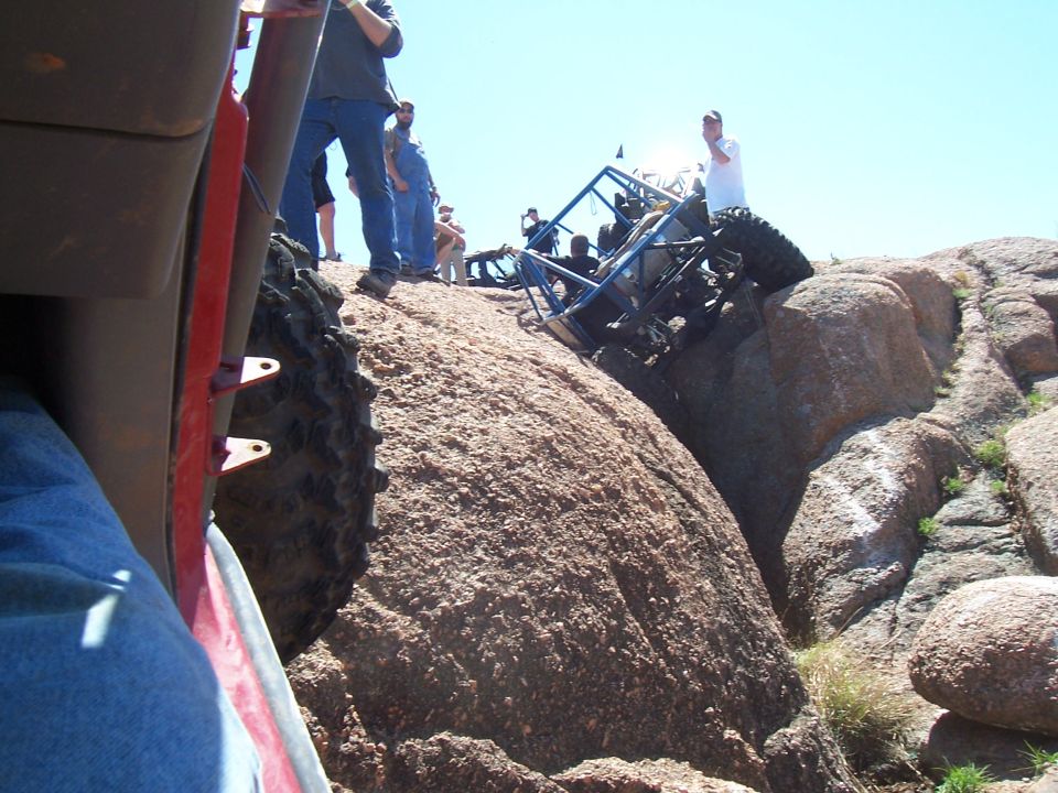 Off-road buggy tipped on its side on a rocky incline with people watching