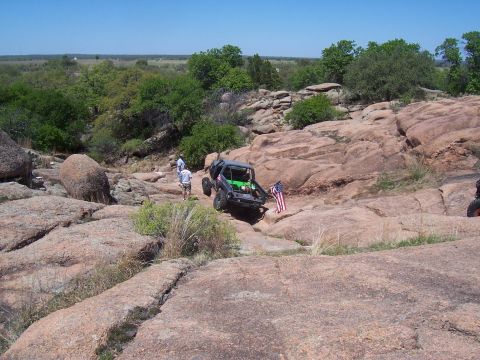 2004 Aston Martin Virage - An off-road vehicle navigates a rocky landscape, adorned with an American flag.