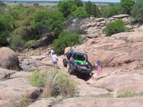 2004 Aston Martin Virage - Off-road vehicle navigates a challenging rocky terrain with an American flag displayed.