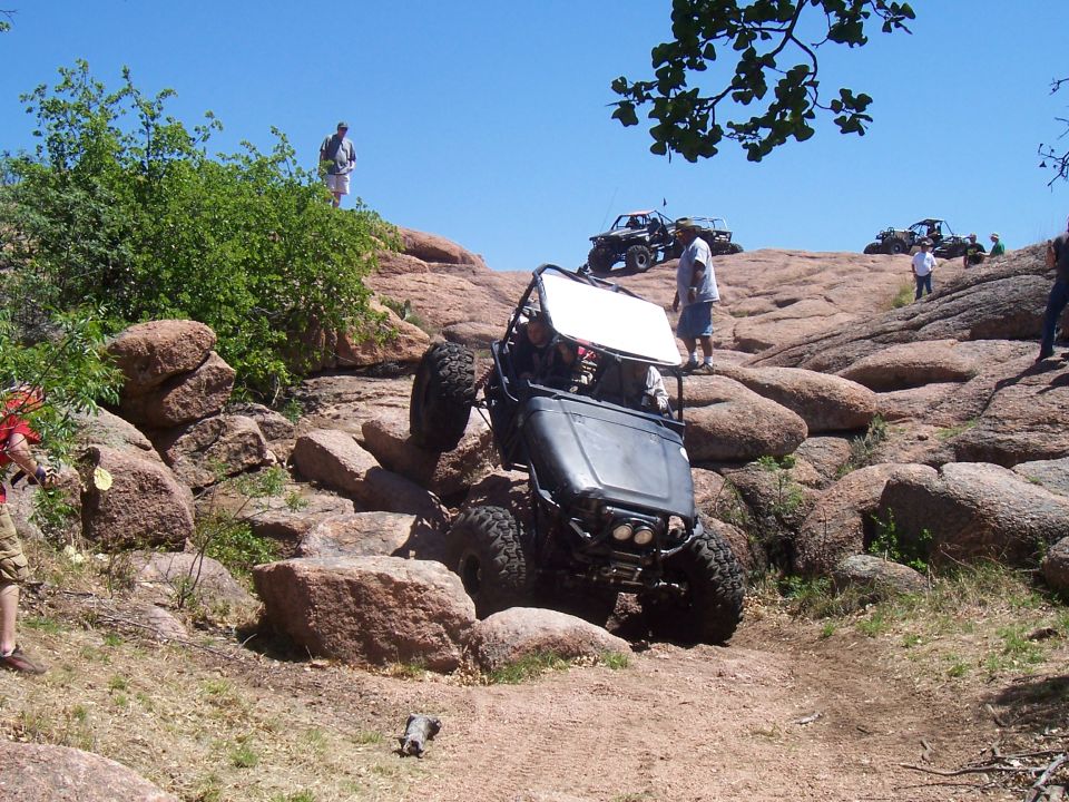 Off-road buggy climbing rocky terrain with other vehicles in background