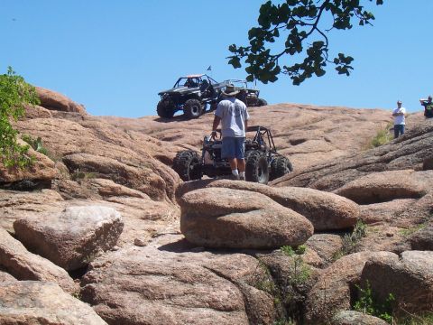 2004 Aston Martin Virage - Several off-road vehicles navigate a steep, rocky landscape on a sunny day.