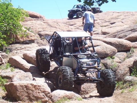2004 Aston Martin Virage - Two off-road vehicles navigate a rocky, uphill terrain under a clear blue sky.