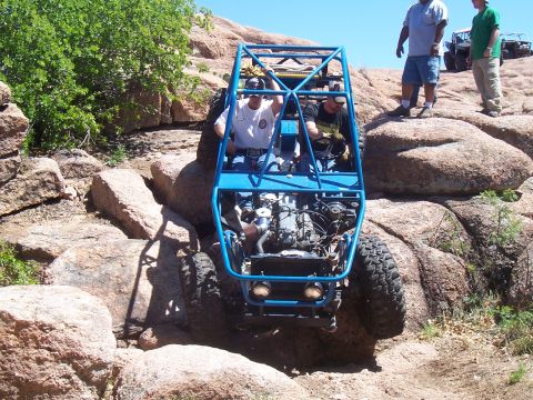 2004 Aston Martin Virage - A blue off-road buggy navigates a challenging rocky trail, with another vehicle and spectators in the background.