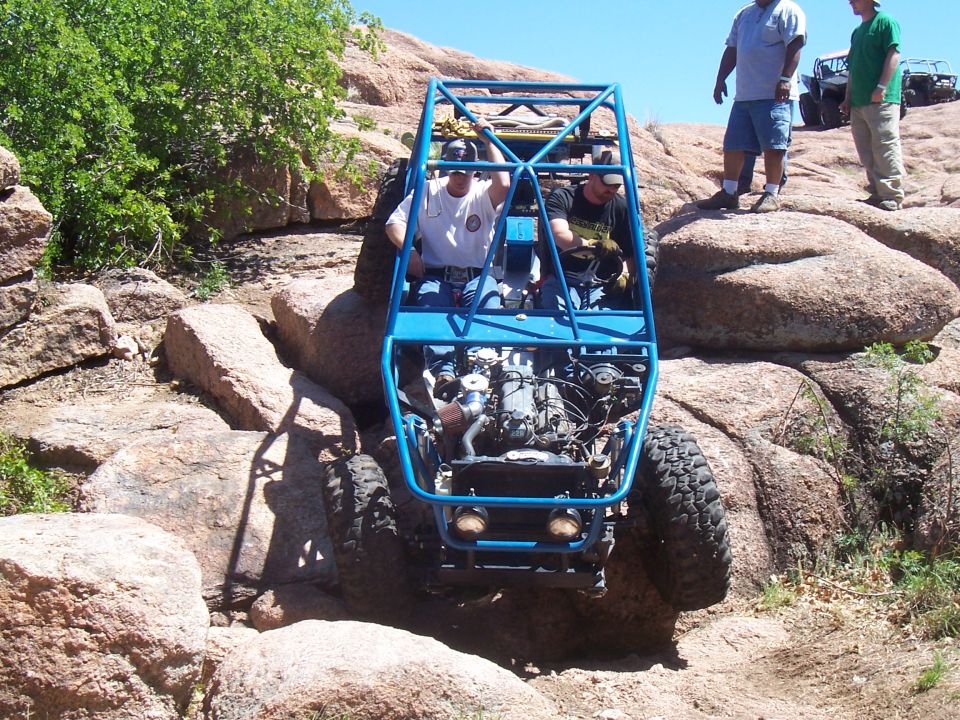 Blue off-road buggy climbing rocks with two occupants; another buggy visible in background