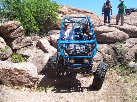 2004 Aston Martin Virage - Two people ride in a custom blue buggy as it climbs over large rocks on a trail.