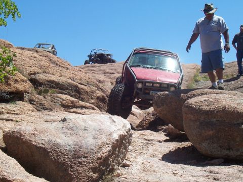 2004 Aston Martin Virage - Multiple off-road vehicles traverse a challenging rocky landscape under a clear blue sky.
