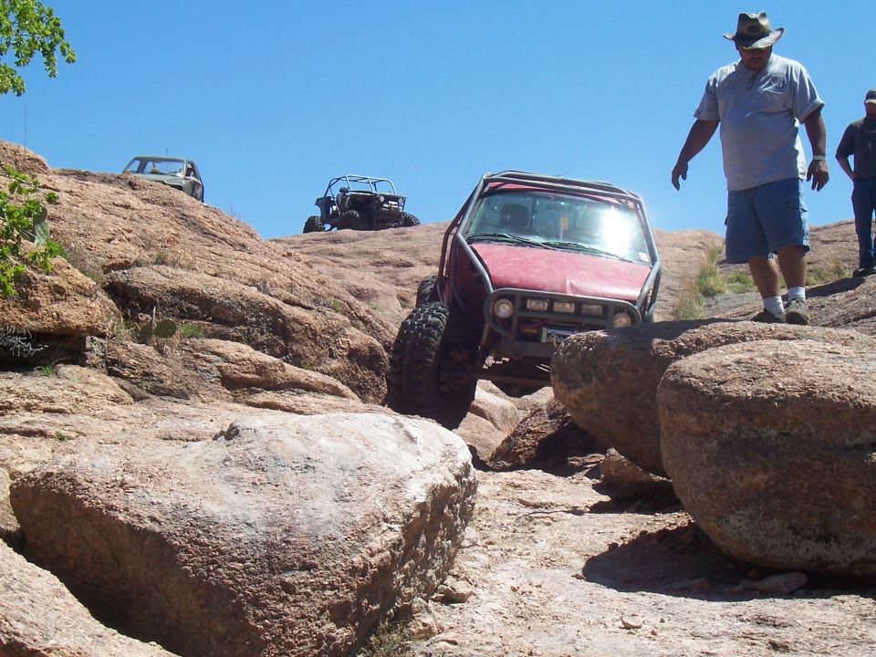 Red off-road vehicle climbing rocks with two people watching