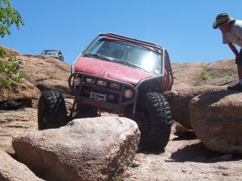 2004 Aston Martin Virage - Modified off-road vehicle tackling a challenging rocky trail with a spectator watching.