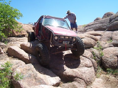 2004 Aston Martin Virage - Modified off-road vehicle navigating a rocky trail with a person standing nearby.