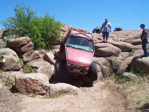 2004 Aston Martin Virage - Multiple off-road vehicles are seen on a rocky landscape under a clear blue sky.
