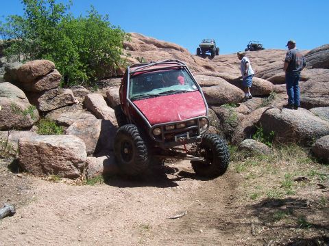 2004 Aston Martin Virage - An off-road vehicle tackles a rocky incline, with other vehicles and spectators present on the terrain.