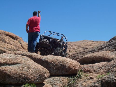 2004 Aston Martin Virage - A person watches an off-road vehicle ascend a challenging rocky slope under a clear blue sky.