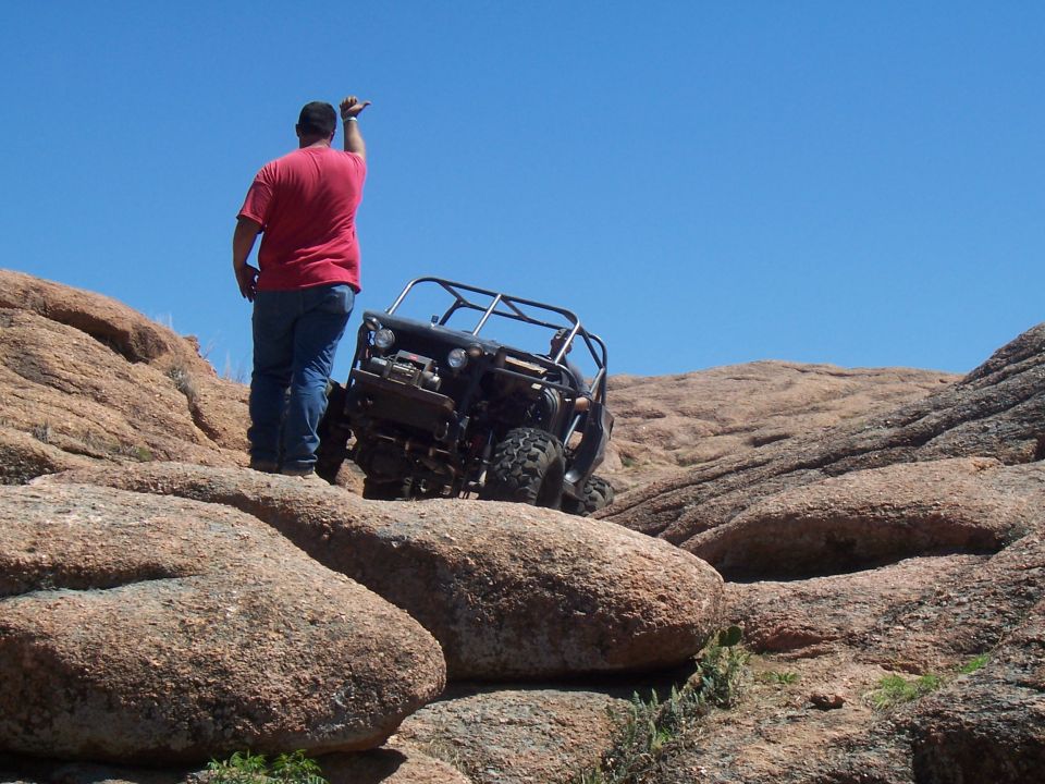 Off-road vehicle navigating a steep, rocky incline with a person standing nearby