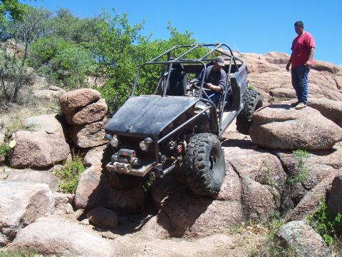 2004 Aston Martin Virage - A driver maneuvers an off-road buggy over challenging rocky terrain with a spectator watching.
