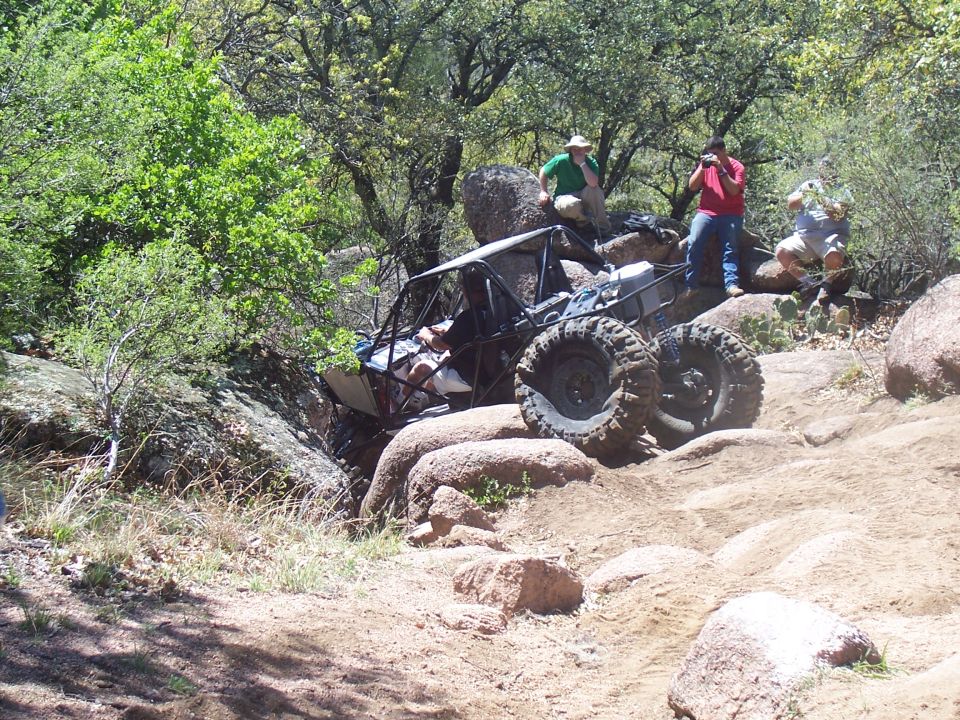 Off-road buggy with large tires climbing over rocks on a dirt trail