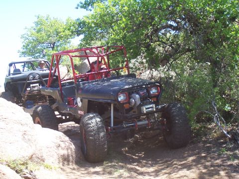 2004 Aston Martin Virage - Two off-road vehicles navigate a challenging rocky path surrounded by trees.