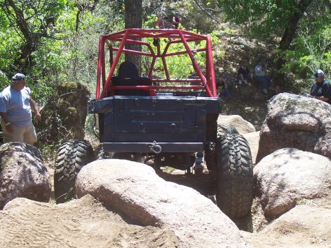 2004 Aston Martin Virage - An off-road buggy with a prominent red roll cage maneuvers through a rocky terrain, with spectators watching from the hillside.