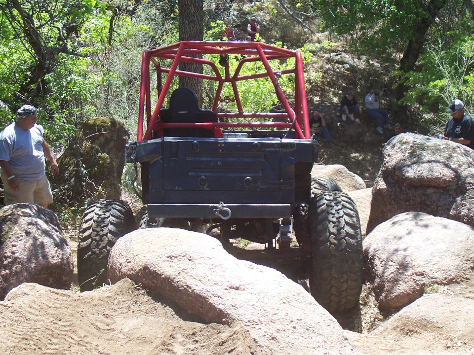 Rear view of a black off-road buggy with a red roll cage navigating large rocks