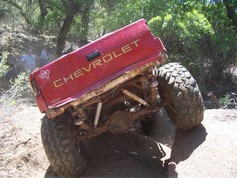 2004 Aston Martin Virage - A modified Chevrolet pickup truck navigates a challenging off-road terrain with its rear end tilted.