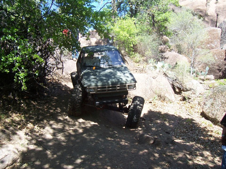 Green off-road vehicle with large tires navigating a rocky trail