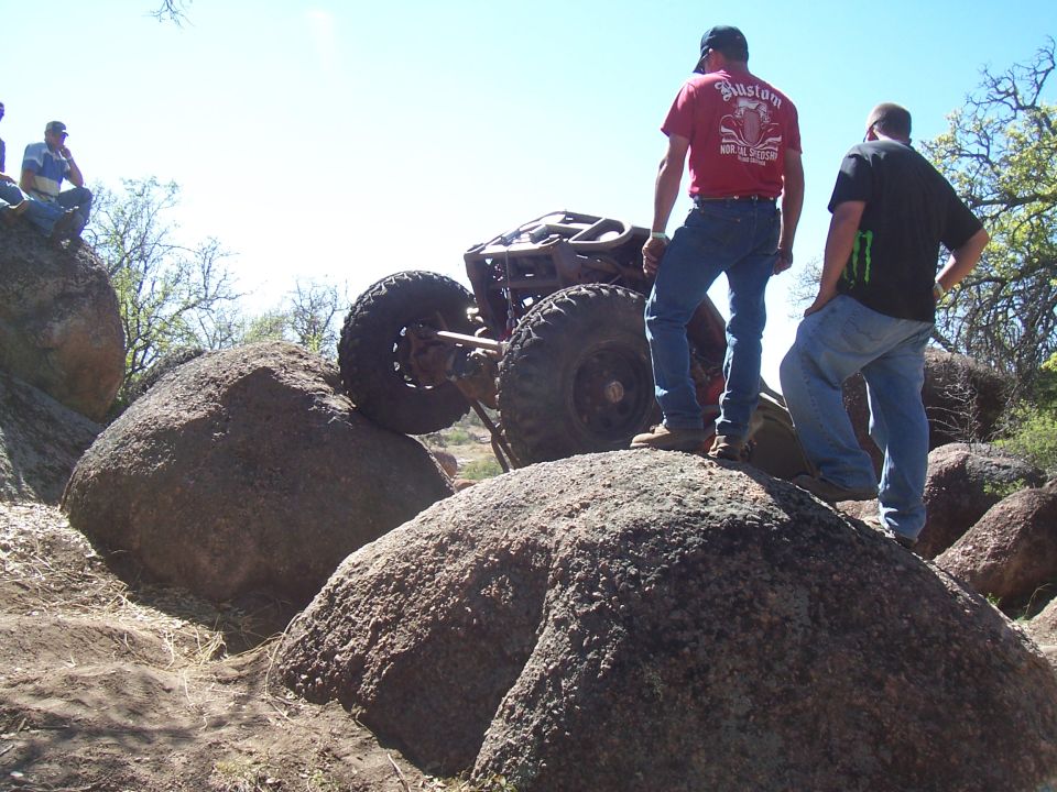 Off-road buggy climbing large rocks, two men watching