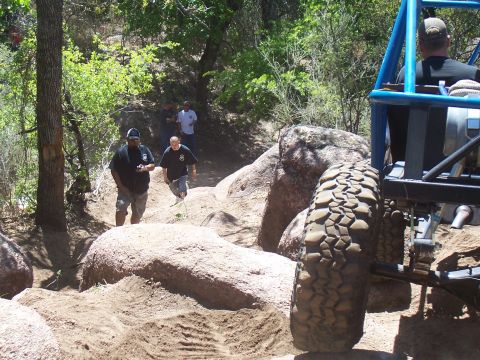 2004 Aston Martin Virage - An off-road buggy tackles a challenging rocky path, with several people observing the action.
